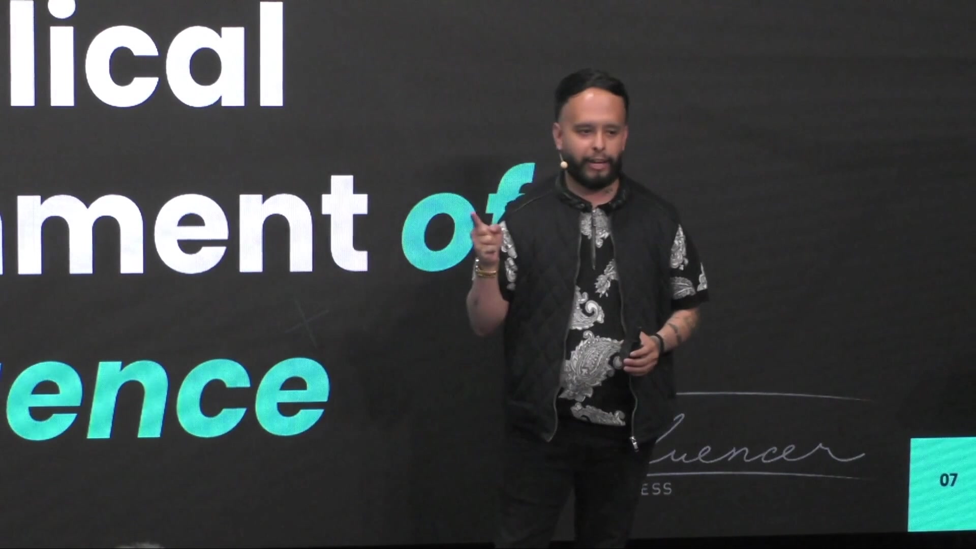 Speaker in a black quilted vest pointing; Influencer Press mark on the slide.